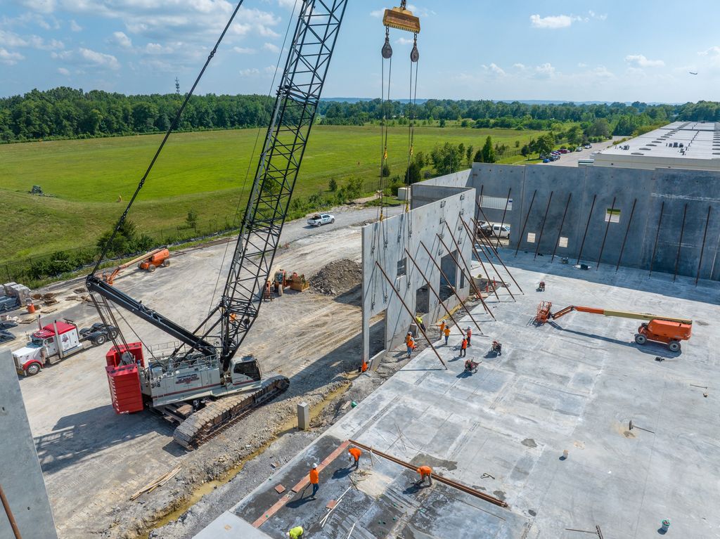 Crawler crane lifting a tilt-up wall panel into place beside open farmland