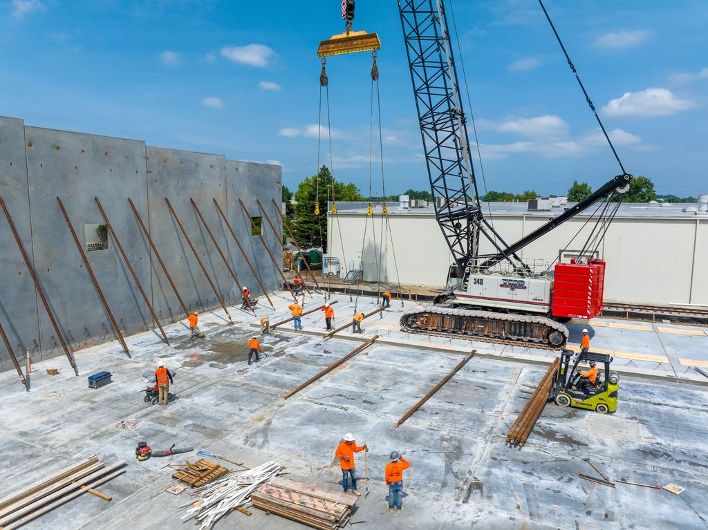 Crew working on a concrete slab as a crawler crane lifts tilt-up wall panels