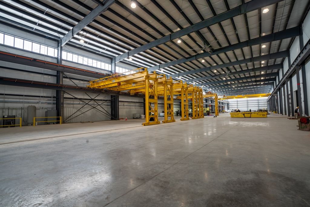 Deep perspective across an empty polished plant floor toward yellow gantry cranes