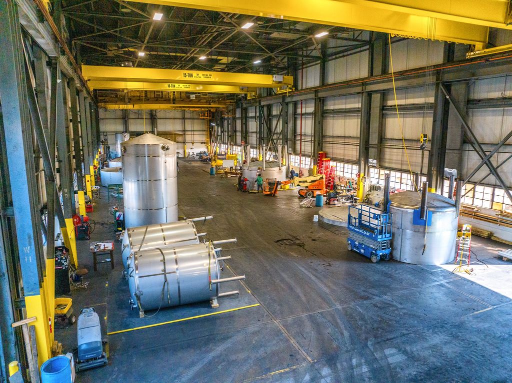 Stainless tanks on a fabrication floor under yellow bridge cranes