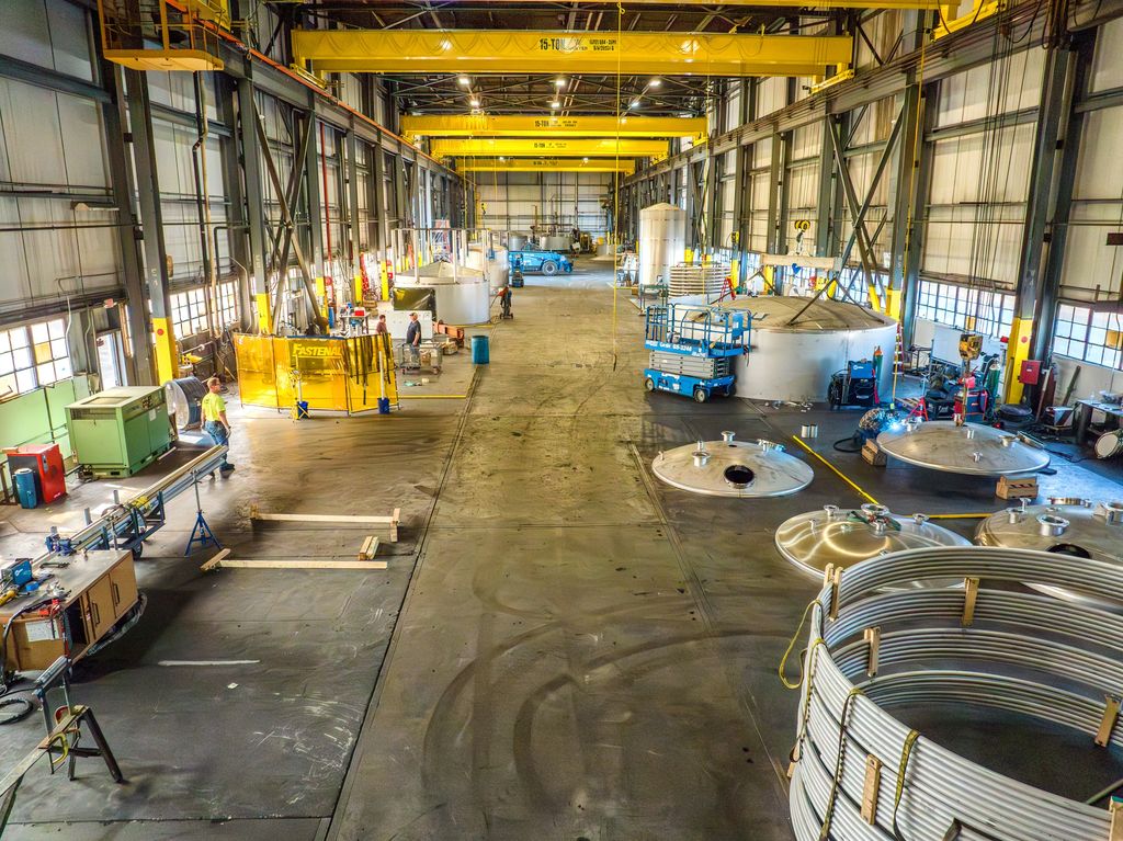Elevated view inside a fabrication plant with yellow overhead cranes and tank sections