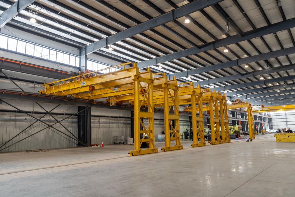 Line of yellow gantry cranes under a steel roof with clerestory windows in a new plant