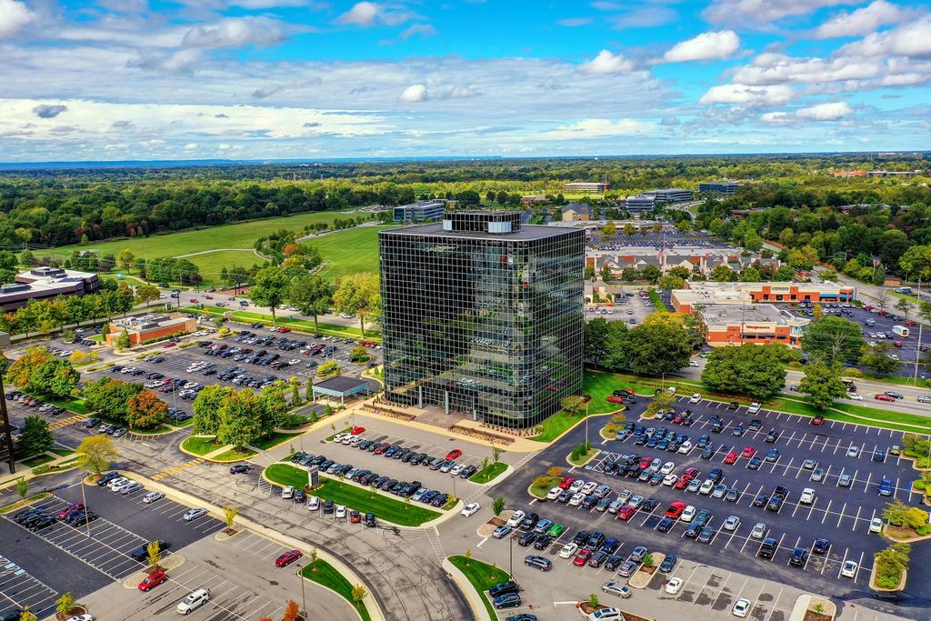 Glass office tower surrounded by parking lots and trees