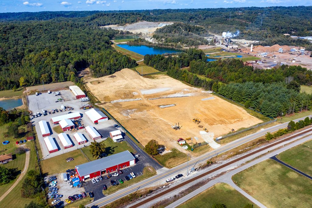 Graded construction site beside storage buildings, a quarry and a rail line