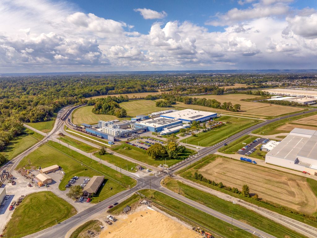 Modern industrial facility at a crossroads surrounded by fields and woods
