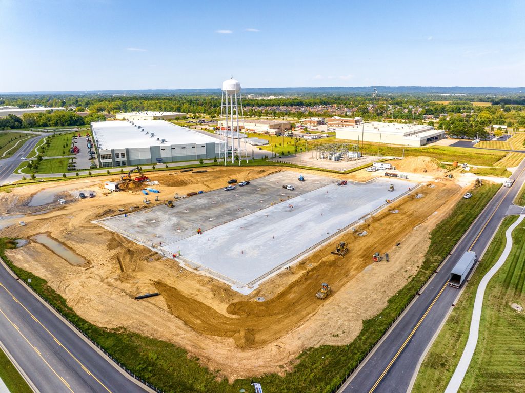 Fresh concrete slab poured on a graded industrial site beside a road and water tower