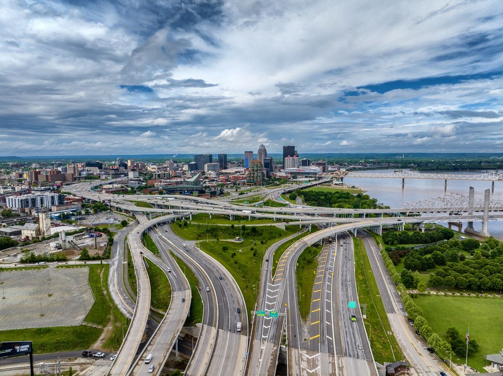 Interstate lanes and overpasses curving toward downtown Louisville under dramatic clouds