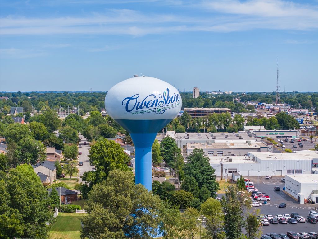Owensboro water tower rising over trees and rooftops on a summer day
