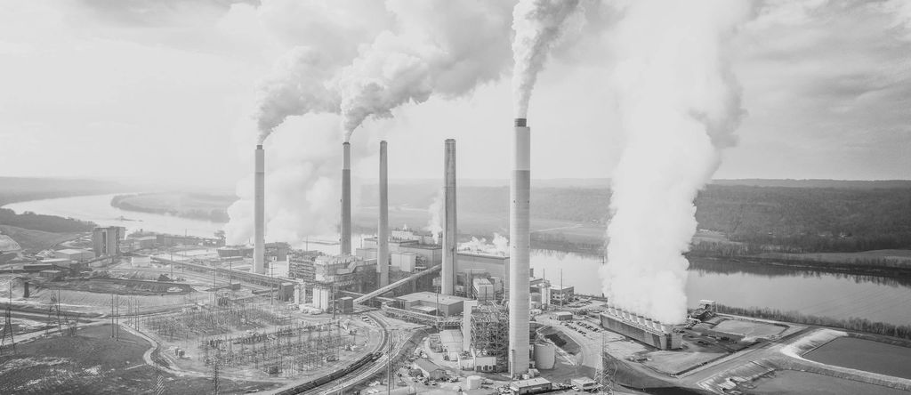 Black and white aerial view of a riverside power plant with four smokestacks releasing steam