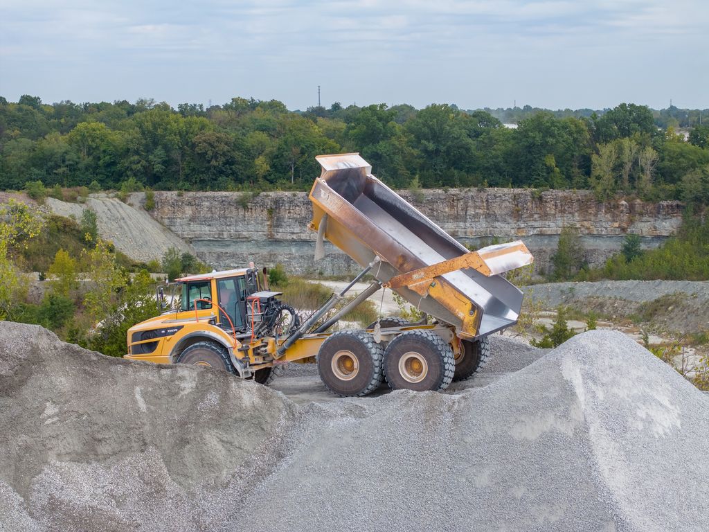 Articulated dump truck unloading crushed stone onto a stockpile in front of a quarry wall
