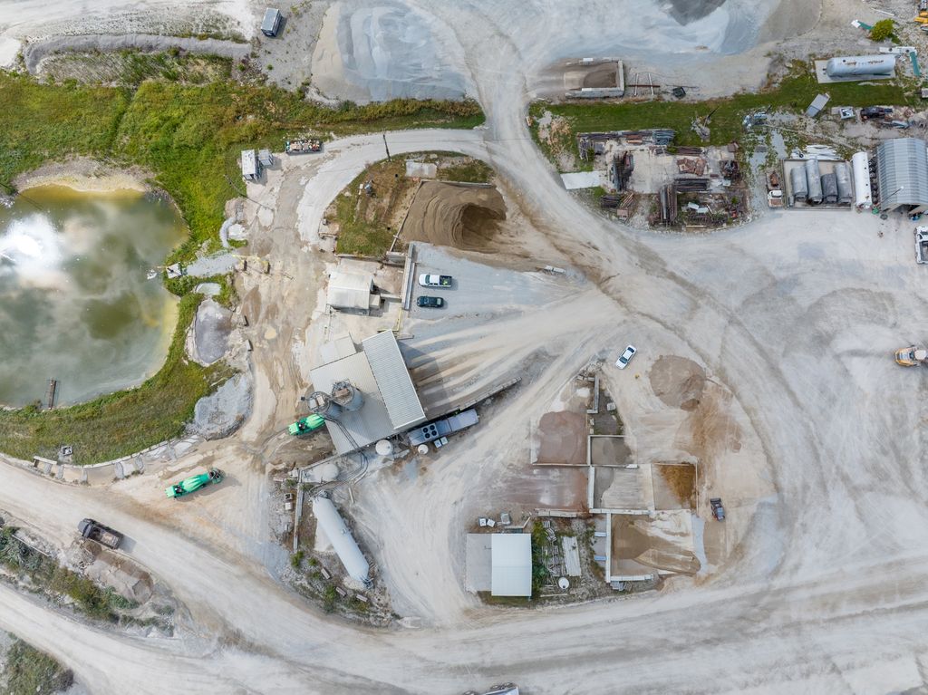 Top-down view of quarry buildings, trucks and a green pond among gravel roads