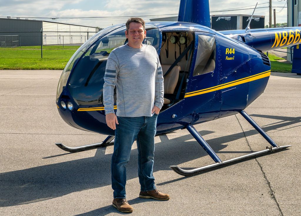 Shaun Wilson, the pilot behind Arrow Aerial, standing beside an R44 helicopter on the ramp