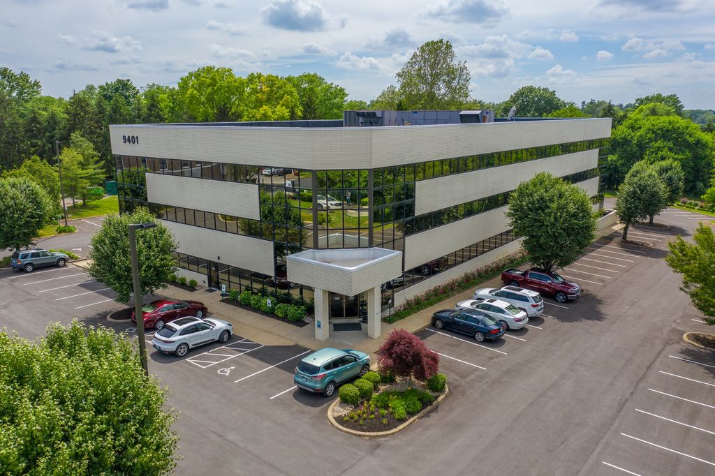 Three-story office building with dark glass bands and a parking lot among mature trees