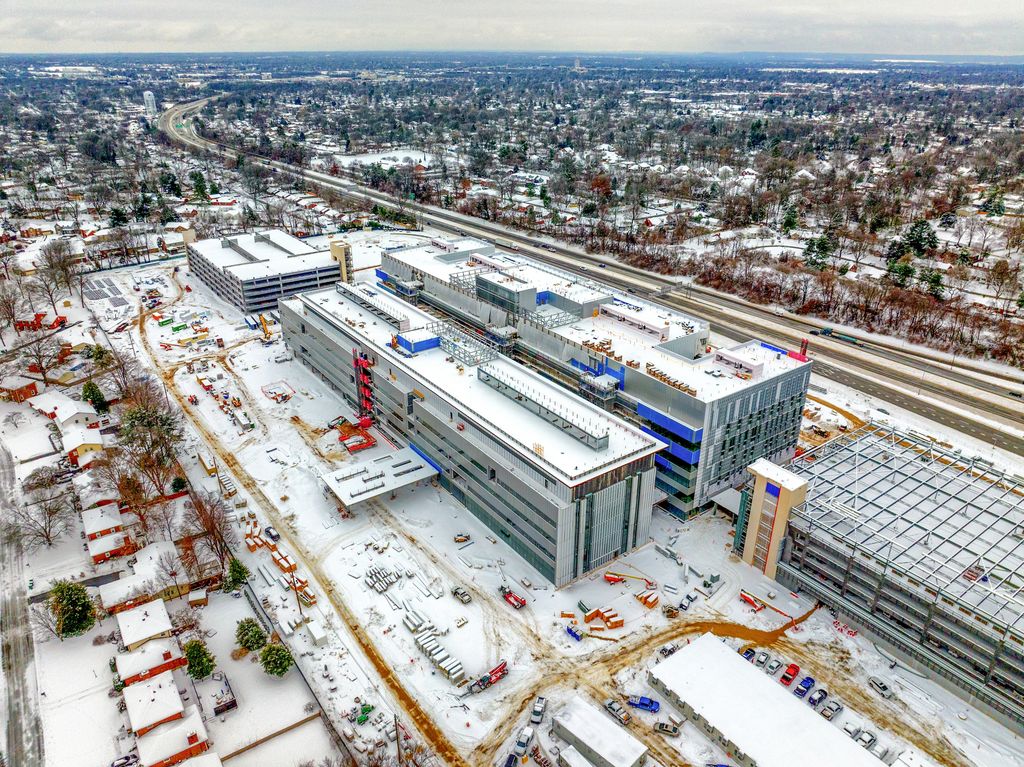 Hospital buildings and a parking garage under construction beside an interstate on a snowy day