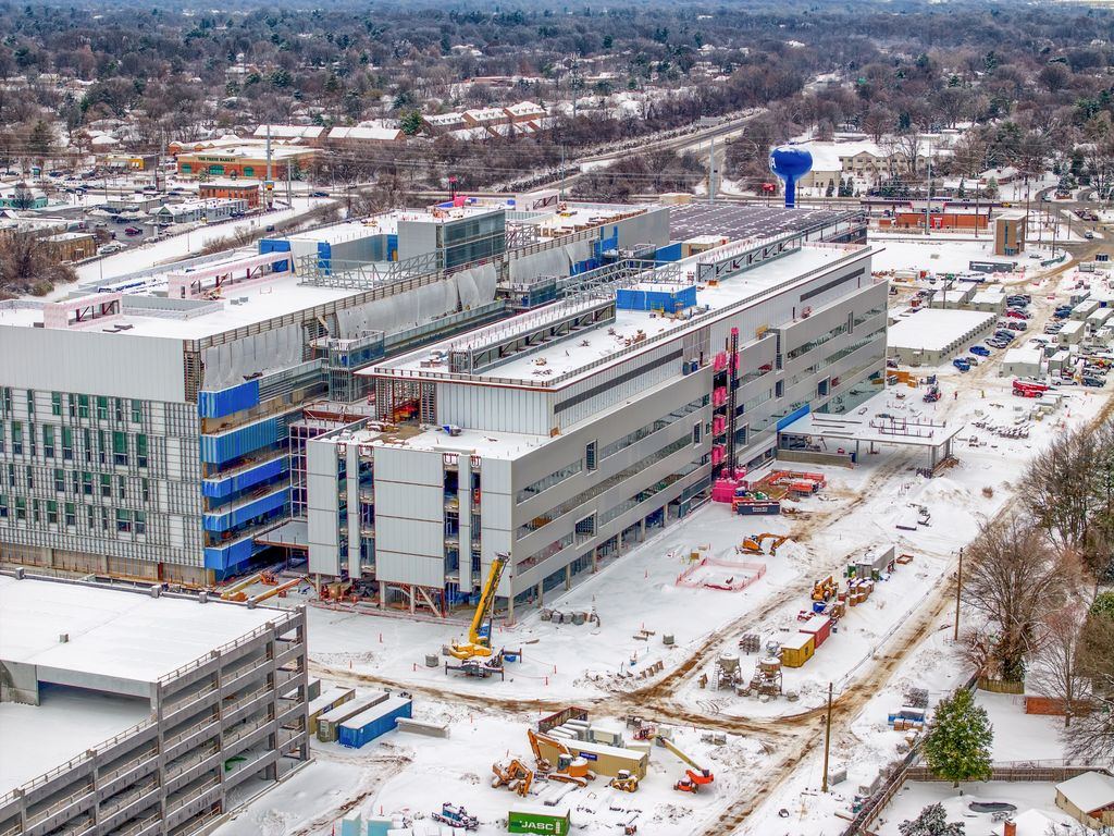 Tower crane and multistory hospital wings under construction near a blue water tower